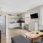 Living kitchen with dining table, fridge, and TV. Wooden floor and large windows.