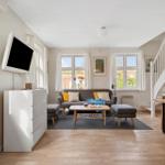 Living room with sofa, coffee table, and TV. Wooden floor and windows with view.