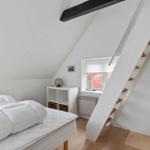 Bedroom with sloped ceiling, bed, window, and stairs.