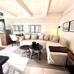 Wohnzimmer mit Sofa, Tischen und Fenstern. Holzmöbel und Wandbilder.