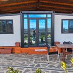 Container house with patio, table and chairs under wooden cover.