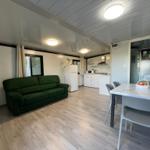 Living room with green sofa, kitchen area, and dining table with chairs.
