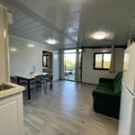 Living area with green sofa, dining table, and kitchenette. View of terrace and landscape.