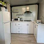 Kitchen with white cabinets, stove, sink, and refrigerator. Wooden floor and plant.