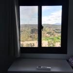 Through the window, you see a hilly landscape with trees and mountains in the background.