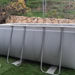 An inflatable pool sits on artificial grass in front of a stone wall.