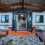Container house with terrace, glass doors, and flower beds. Stone floor and wooden steps.