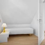 Schlafzimmer mit Dachschrägen, weißem Bett und Nachttisch mit gelber Lampe.