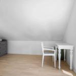 Ein Zimmer mit schrägen Wänden, einem weißen Schreibtisch und Stuhl sowie einem grauen Schrank.