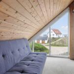 Ein grauer Sofa unter einer Holzdecke mit Blick auf eine Straße und Häuser.
