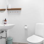 Badezimmer mit Toilette, Waschbecken und Holzregal an der Wand.