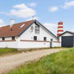 Wohnhaus mit rotem Dach und weißer Fassade, daneben steht ein roter Leuchtturm.