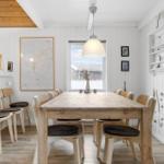 Esszimmer mit Holztisch, Stühlen und Fensterblick. Weiße Wände, Holzdecke und Küchenzeile.