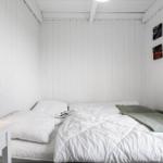 Schlafzimmer mit weißer Wandverkleidung, Bett mit weißen Kissen und Decke, Wandlampen und Bildern.