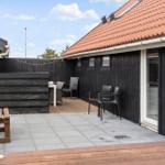 Terrasse mit Tisch, Stühlen und Holzbank vor schwarzem Haus mit rotem Dach.