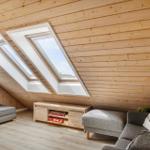 Wohnraum mit Holzwand, Dachfenstern und grauer Sofa-Ecke.