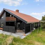 Ein schwarz gestrichenes Haus mit rotem Dach, Terrasse und Schaukel im Garten.