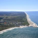 Aerielansicht einer Küstenlandschaft mit Strand, Meer und Siedlung.