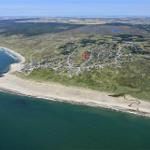 Aerial view of a coastal village with beach and surrounding green landscape.