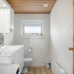 Badezimmer mit Waschbecken, Toilette und Fenster. Holzdecke und Tür.