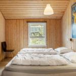 Schlafzimmer mit Holzwand, Bett, Fenster und Deckenleuchte.