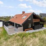 Modernes Haus mit Terrasse, Holzveranda und rotem Dach. Umgeben von Gras und weiteren Häusern.