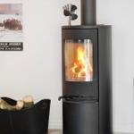 Black wood-burning stove with burning logs, fire tools on wall beside it.