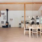 A room with dining area, kitchen, and fireplace. Wooden floor and ceiling beams.