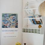 Wall with art poster, shelf with plates and books, wooden surface with vase and bottle.