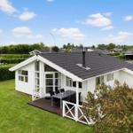 Weißes Ferienhaus mit Terrasse und Garten unter blauem Himmel.