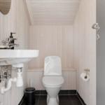 Badezimmer mit Toilette, Waschbecken und Spiegel an Holzwand.
