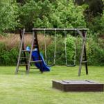 Hinterhof mit Holzschaukel, blauer Rutsche und Spielplatzfläche.
