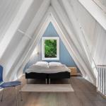 Schlafzimmer mit Dachschrägen, blauer Wand und Fenster. Bett, Stuhl und Teppich sind sichtbar.