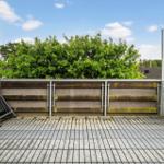 Terrasse mit Holzgeländer und Blick auf grüne Bäume unter blauem Himmel.