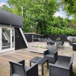 Terrasse mit Gartenmöbeln, Tisch, Liegen und Hängematten. Holzdeck und grüne Bäume im Hintergrund.
