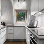 Küche mit weißen Schränken, Arbeitsplatte und Fenster. Kühlschrank und Spüle sichtbar.