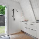 Eingangsbereich mit weißen Wänden, Garderobe und Küchenzeile. Tür führt nach draußen.