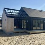 Moderne Strandvilla mit Holzfassade und großzügigem Glasbereich.