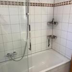 Bad mit Dusche und Badewanne, weiße Fliesen und Chromhalterungen.
