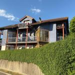 Ein zweistöckiges Haus mit Balkonen und Dachterrasse, umgeben von grüner Hecke.