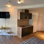 Küche mit Arbeitsplatte, Spüle und Mikrowelle. Esstisch mit zwei Stühlen. TV an der Wand.