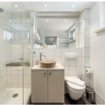 Badezimmer mit Dusche, Waschbecken und Toilette. Weiße Fliesen und Spiegel.