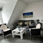 Wohnzimmer mit Sofa, zwei Sesseln und Couchtisch unter schrägen Dachdecken.