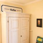 Haus mit Kleiderschrank, Wandbildern und Schild Koffer.