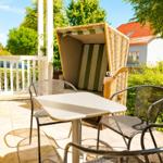 Terrasse mit Tisch, Stühlen und Strandkorb. Grün umgebene Außenterrasse mit Blick auf Haus.