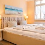 Schlafzimmer mit Bett, Wandbild und Fenster mit Vorhängen.
