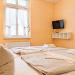 Zwei Betten mit Bettwäsche, Fernseher und Fenster mit weißen Vorhängen.