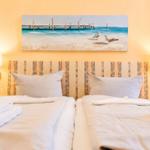Zwei Betten mit weißen Bettwäsche und Handtüchern. Wandbild zeigt Strand und Pier.