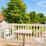 Balkon mit Tisch und zwei Stühlen. Blick auf grüne Bäume und einen Garten.
