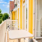 Terrasse mit Tisch und Stühlen, gelbe Fassade und Blick auf grüne Bäume.